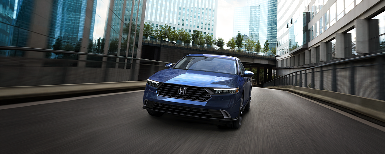 Plan avant d’une Accord bleue roulant vers la caméra dans une rue urbaine vide au milieu de bâtiments.