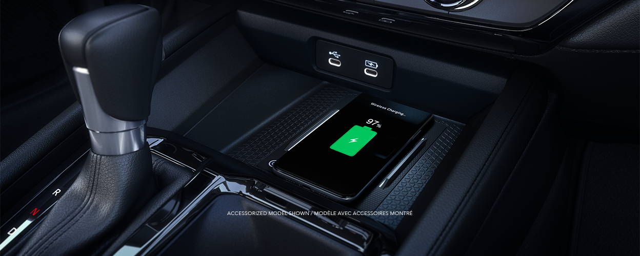 Gros plan d’un téléphone intelligent compatible qui se recharge sans fil sur le tapis de recharge devant le levier de vitesses.