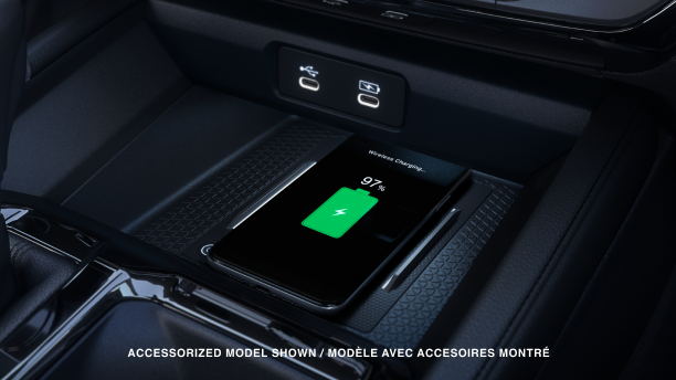 Gros plan d’un téléphone intelligent compatible qui se recharge sans fil sur le tapis de recharge devant le levier de vitesses.