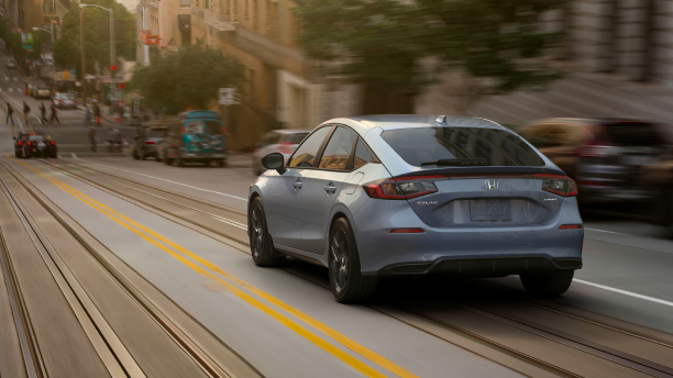3/4 rear view of blueish grey Hatchback driving downhill on city road at dusk.