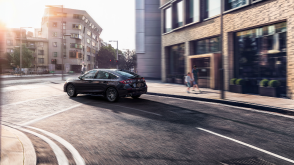 3/4 side rear view of black Hatchback taking a turn on a city street, in morning light. 