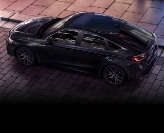 3/4 bird’s eye view of black Hatchback parked on brick city road.