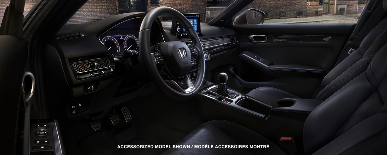 3/4 interior close up of front seats and cockpit. Outside the windows we see a brick wall in an old warehouse district.