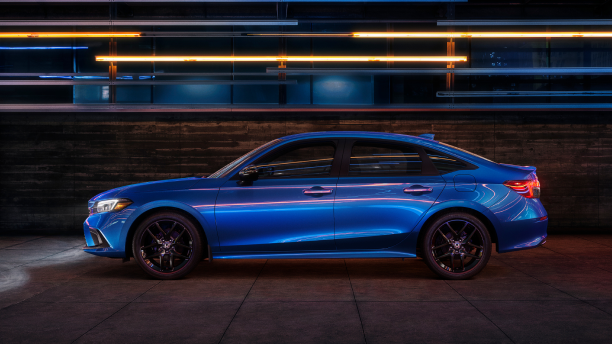 Side view of a parked blue Civic Sedan in a dark warehouse-like space. 