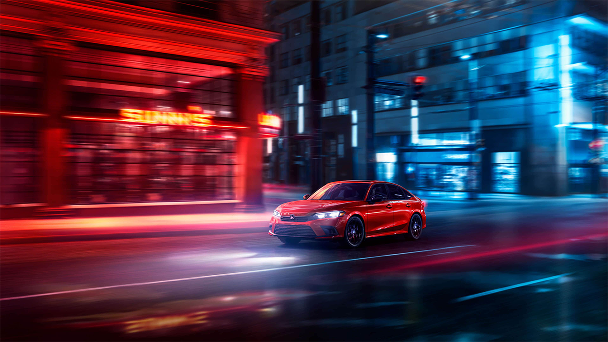 Plan de trois quarts de l’avant d’une Civic berline rouge en ville pendant la nuit.