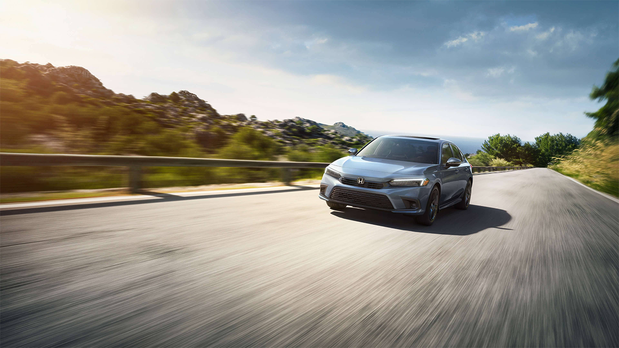 Front view of a grey Civic Sedan driving toward camera on an oceanside highway.