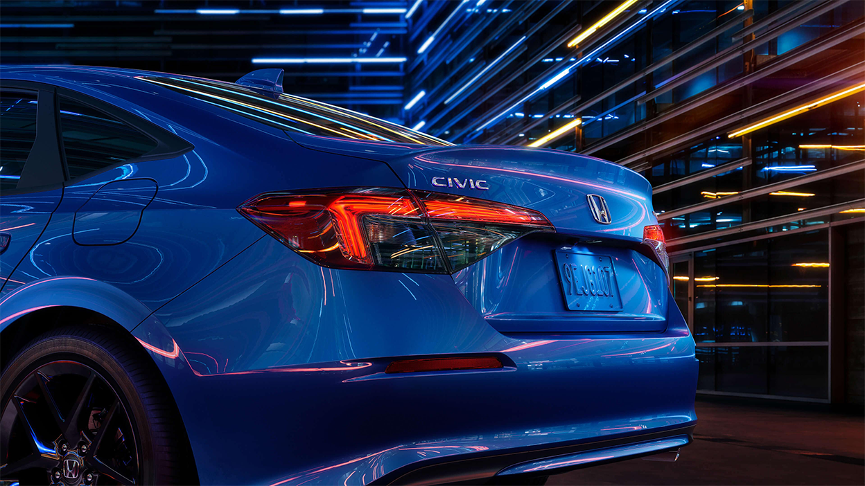 Gros plan de trois quarts du feu arrière et du coffre d’une Civic berline bleue dans un espace sombre comme un entrepôt.