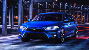 3/4 front view of a parked blue Civic Sedan in a dark warehouse-like space.