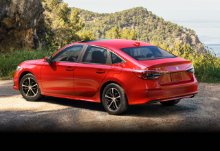 3/4 side rear view of red Civic Sedan parked at a scenic lookout spot overlooking plush green hills.