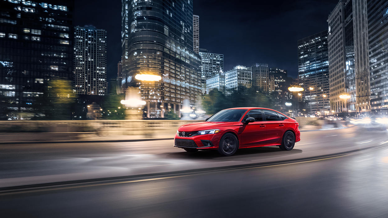 Vue latérale avant de trois quarts d’une Civic Si rouge circulant en ville la nuit.
