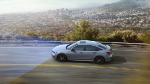 3/4 bird’s eye sideview of a greyish blue Civic Si driving highway overlooking a city. Blue sensor lines emit from the front. 