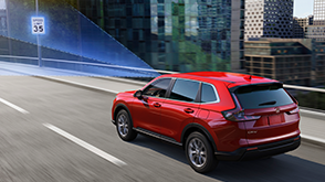 3/4 rear view of red CR-V driving over city bridge. Blue sensor lines emit from the front, detecting the traffic sign ahead. 