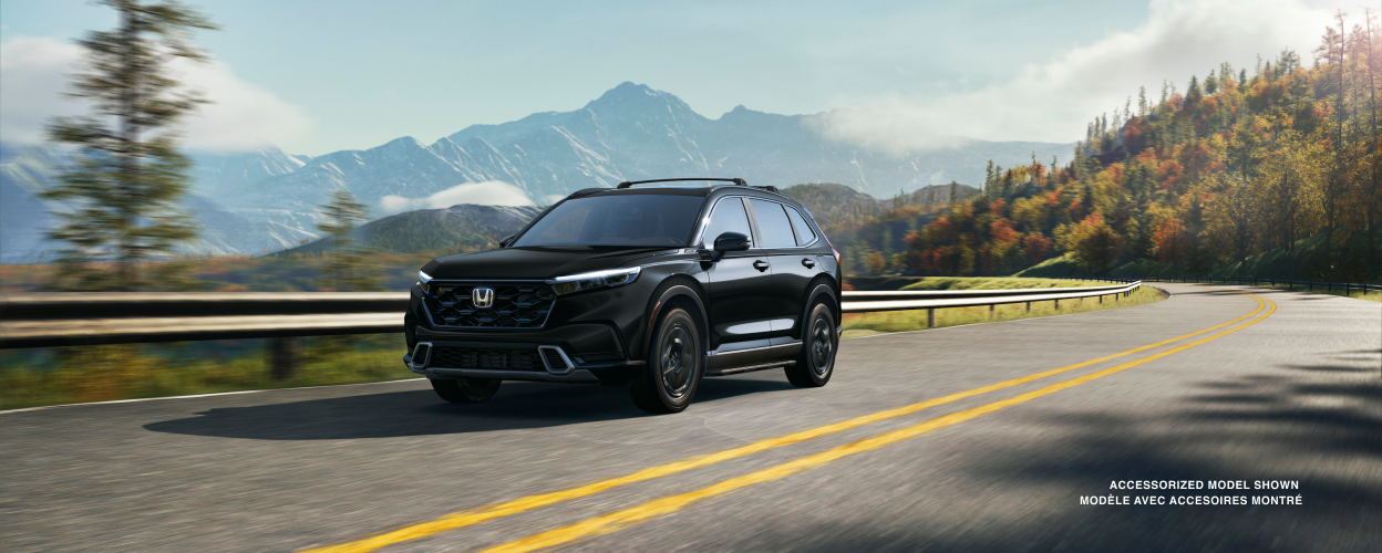 3/4 front view of black CR-V driving on a winding forest highway with fall-coloured trees and mountain range as backdrop. 