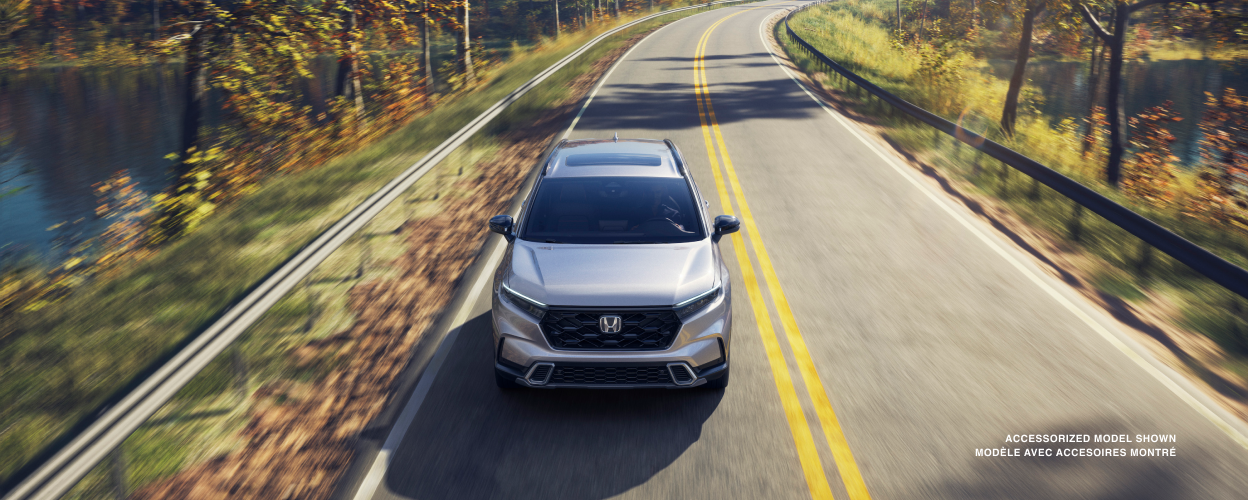 3/4 front bird’s eye view of grey CR-V driving toward camera on a lakeside highway.