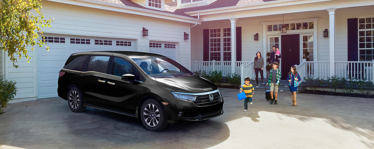 3/4 front side view of black Odyssey parked in driveway. Family walking toward it.