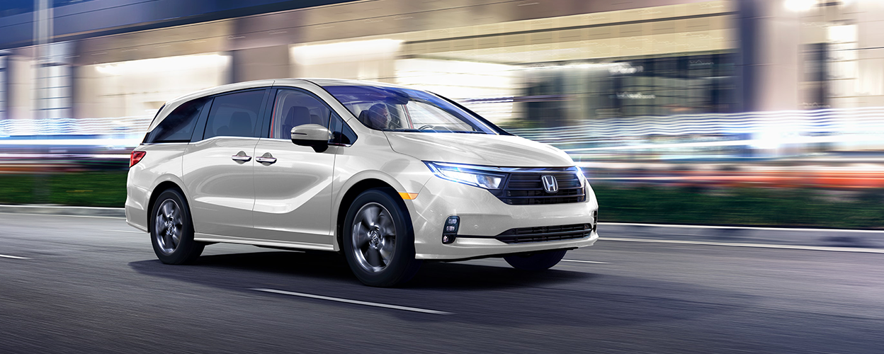 "3/4 side front view of white Odyssey driving on city street at night. "