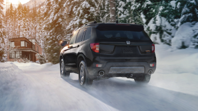 3/4 rear view of black Passport driving on snowy forest road.