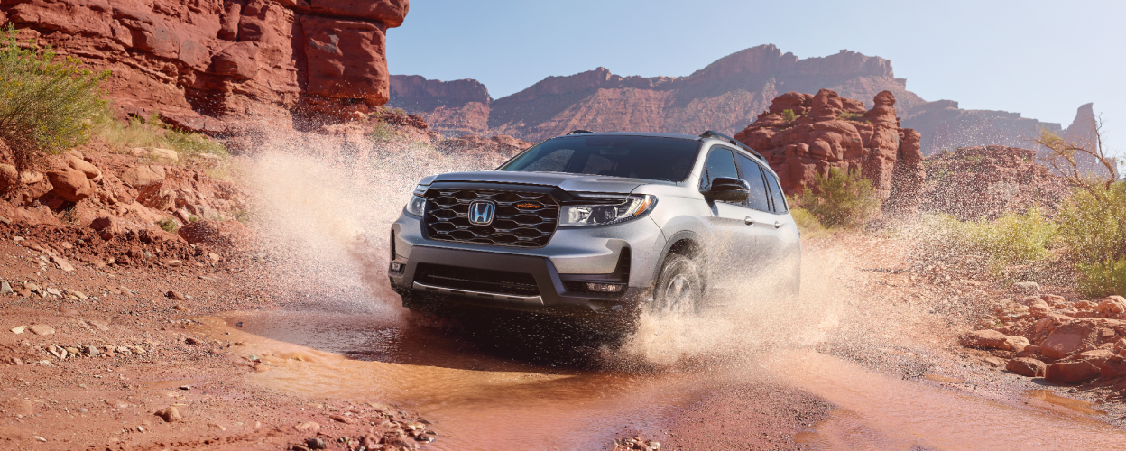 3/4 front view of grey Passport plowing through water on desert trail.