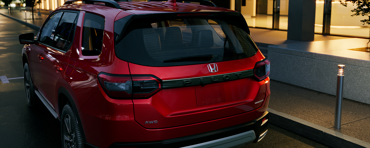 3/4 rear view close up of red Pilot parked curbside in the city at night.