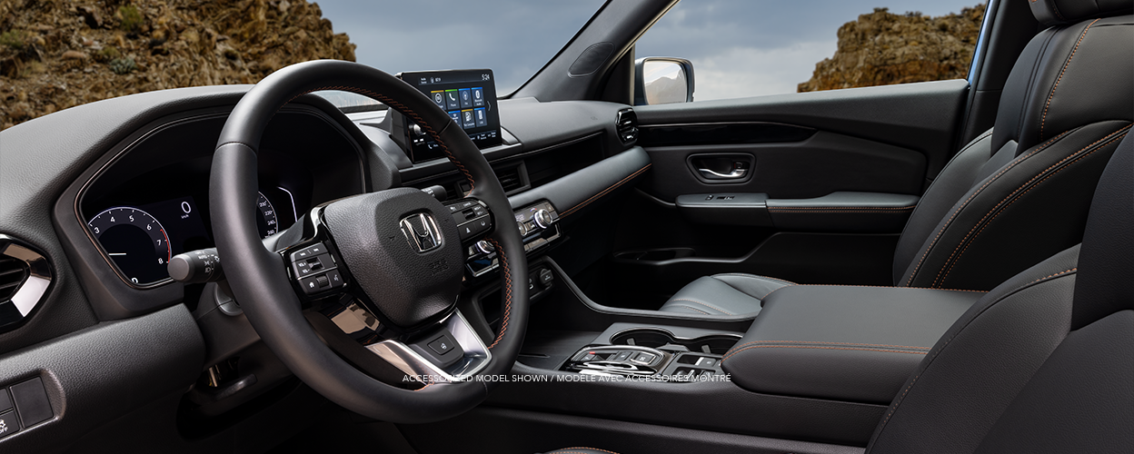 3/4 side view of front seats on a Pilot TrailSport, showcasing its orange stitching and front dashboard.