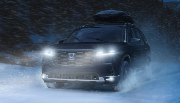 3/4 front view of black Pilot blasting through snow on a snowy forest road.