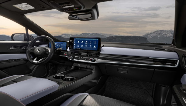 Panoramic interior view of steering wheel, dashboard, and front console. Out the windshield we see snowy mountaintops.