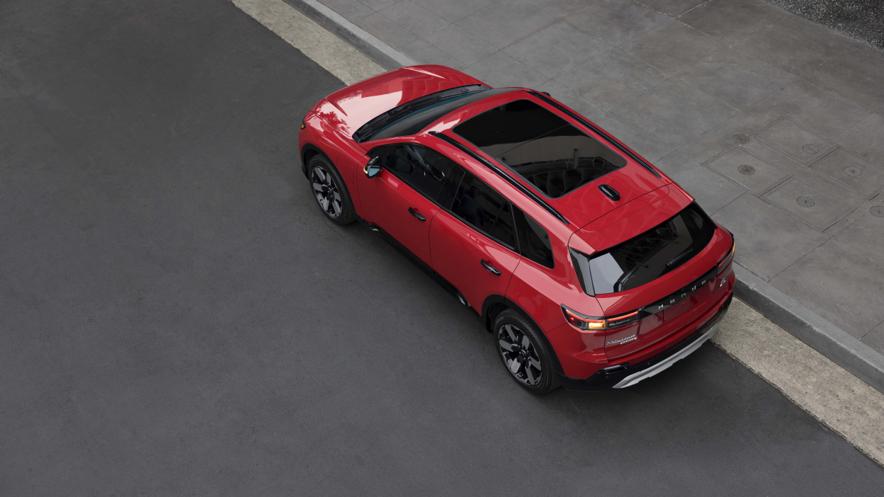 3/4 rear bird's eye view of red Prologue parked curbside on a city street. 
