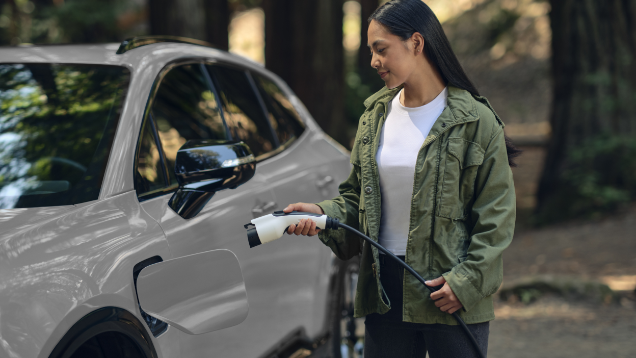 View of a woman plugging in a charging cord into a white Prologue in temperate forest.