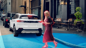 Rear view of a Prologue parked curbside in the city. Blue sensor waves emitting from the back, detecting a woman crossing behind it.
