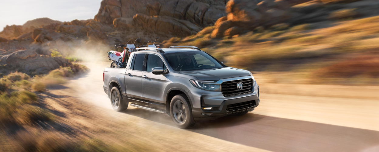 3/4 front view of grey Ridgeline driving on desert road with two motocross bikes in truck-bed.