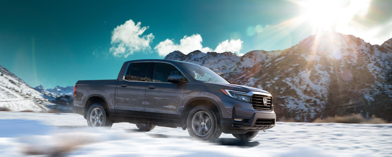 3/4 side view of Ridgeline driving amid snowy mountains.