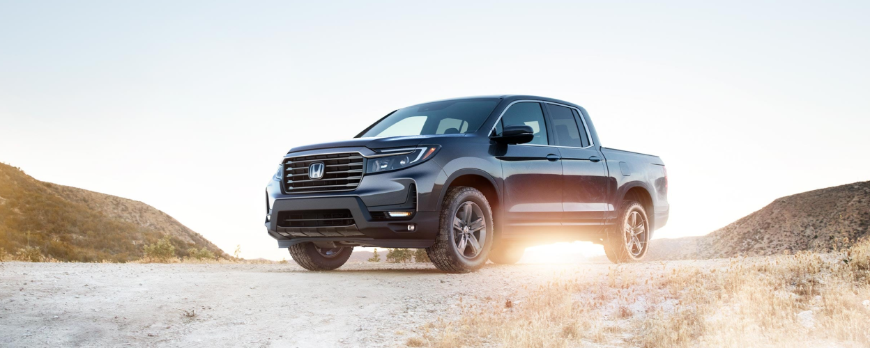 3/4 rear view of grey Ridgeline parked on dirt road.