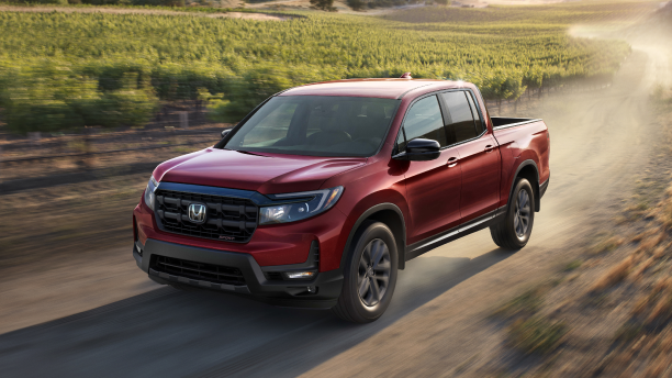 3/4 front view of red Ridgeline driving on dirt road in wine country.
