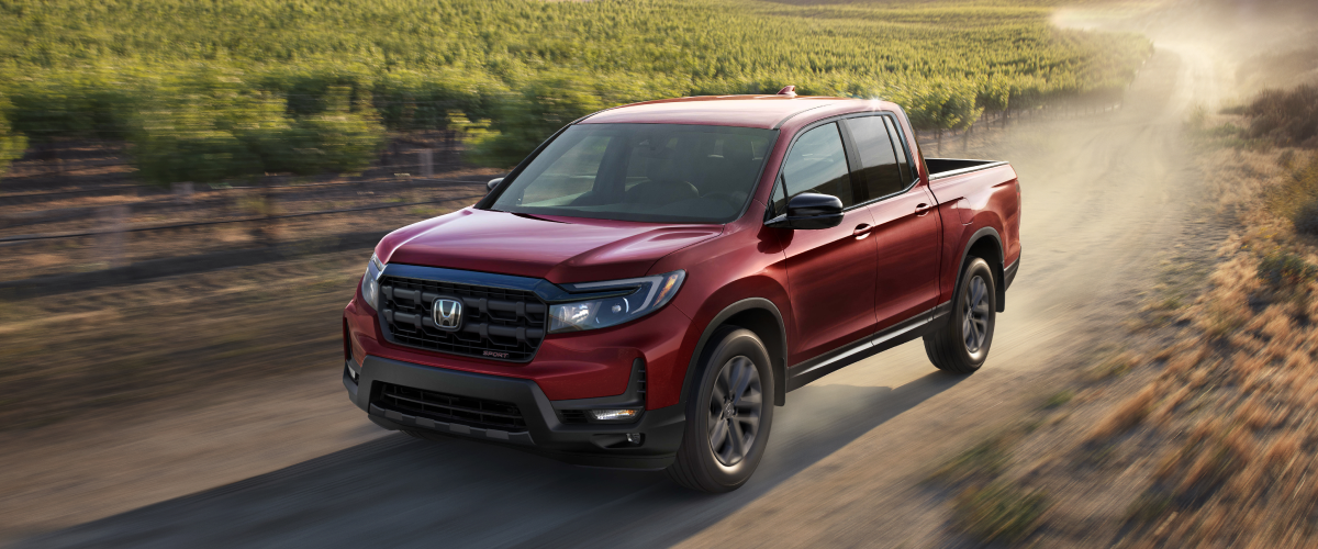 3/4 front view of red Ridgeline driving on dirt road in wine country.