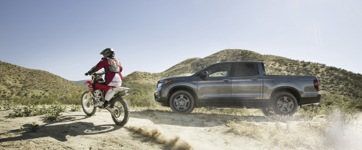 Side view of grey Ridgeline on desert hills with motocrosser on the left.
